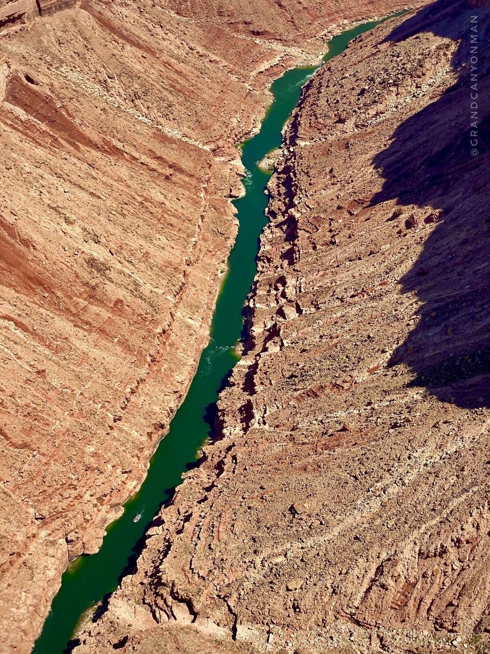 Deep canyon with a vibrant green river snaking through it, shot from above.