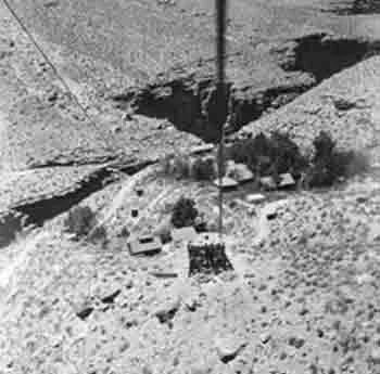 Aerial view of a settlement in a canyon; buildings and trees are visible, with a tower in the foreground.