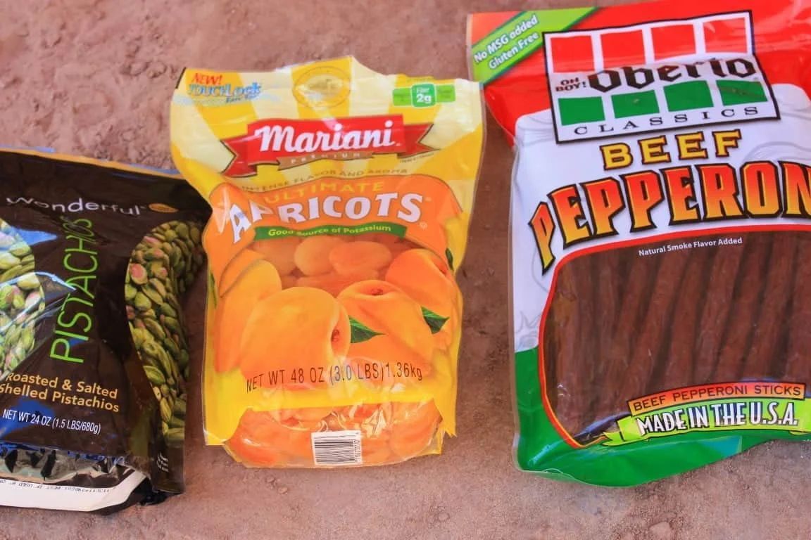 Close-up of four snack packages: pistachios, dried apricots, and beef pepperoni sticks.