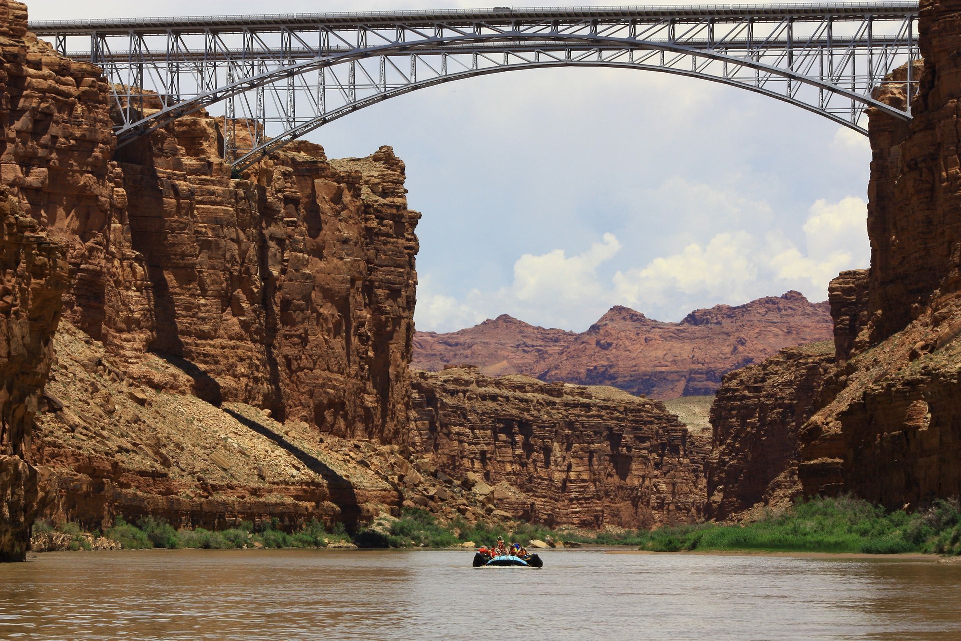 Bridge over a river through a canyon with a boat, brown cliffs, and blue sky.