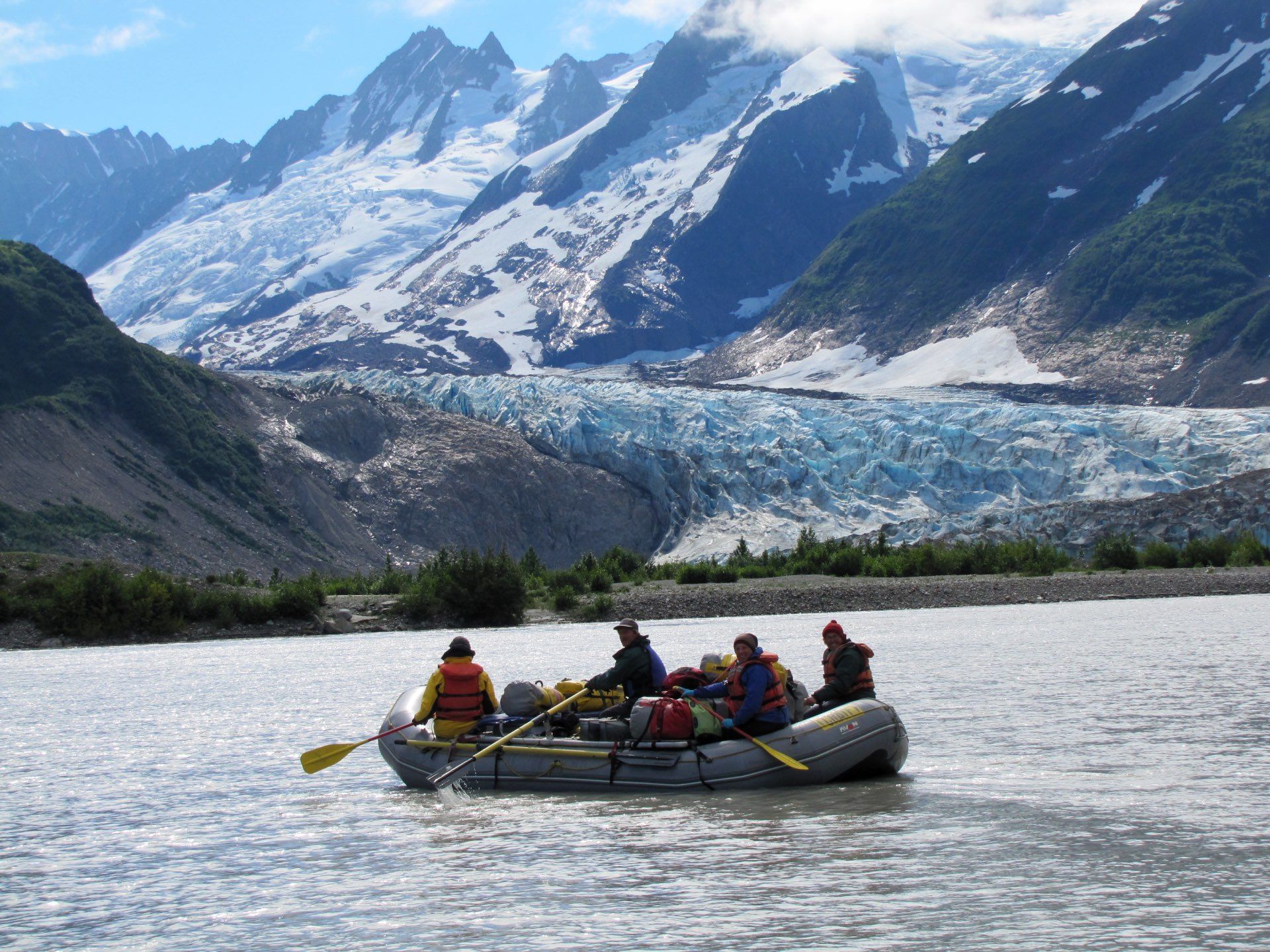 Rafting on a river with mountains and glacier in background. People paddle on a raft.