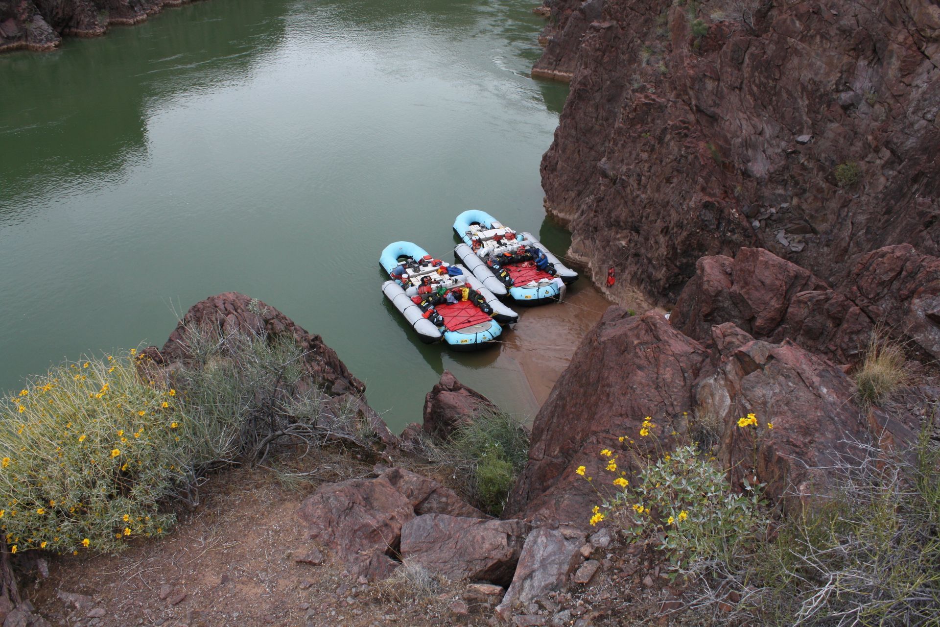 Two rafts on a river near brown rock cliffs and banks, green water.