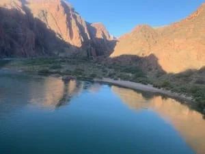 Calm turquoise water reflects reddish canyon walls under a clear, blue sky.