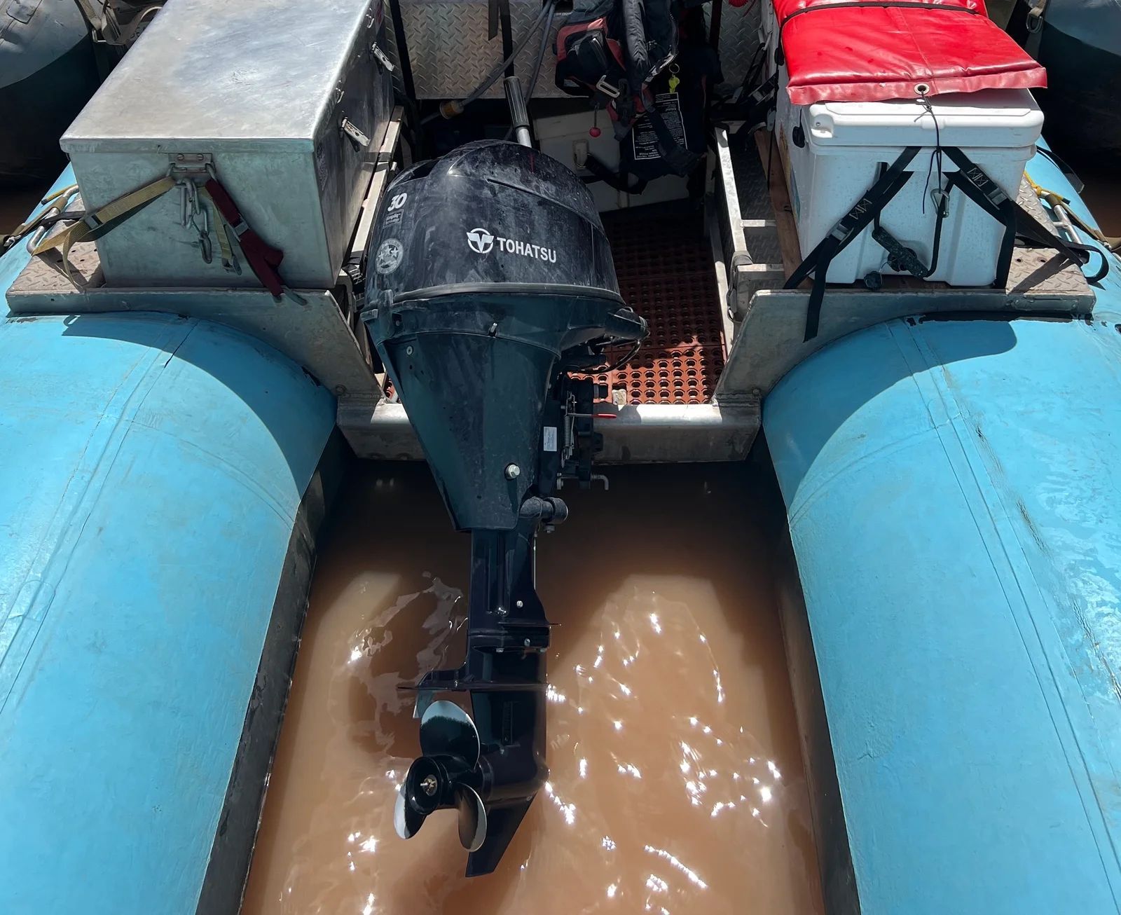 Blue inflatable boat with black motor in murky water.