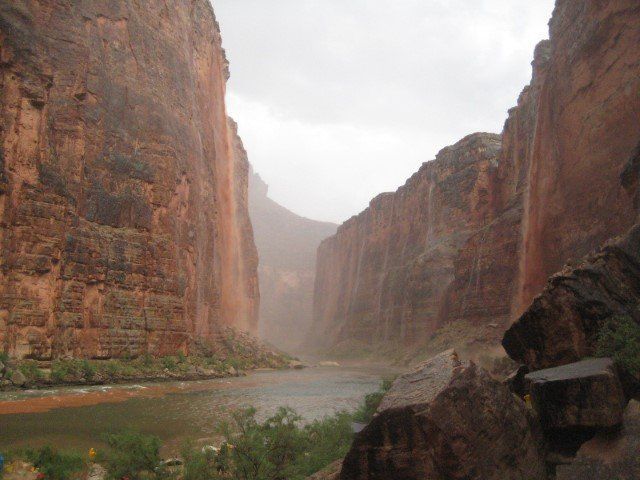 River flowing through a deep canyon of red rock walls on a cloudy day.