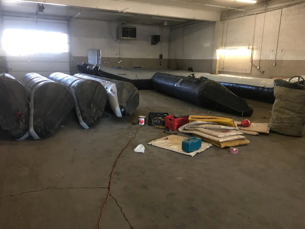 Warehouse interior with bundled inflatable rafts and scattered tools on concrete floor.