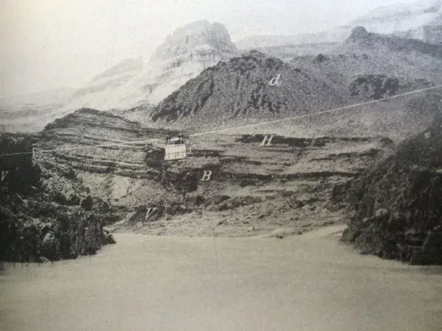 Black and white photo of a canyon with a body of water in the foreground and mountains in the background.