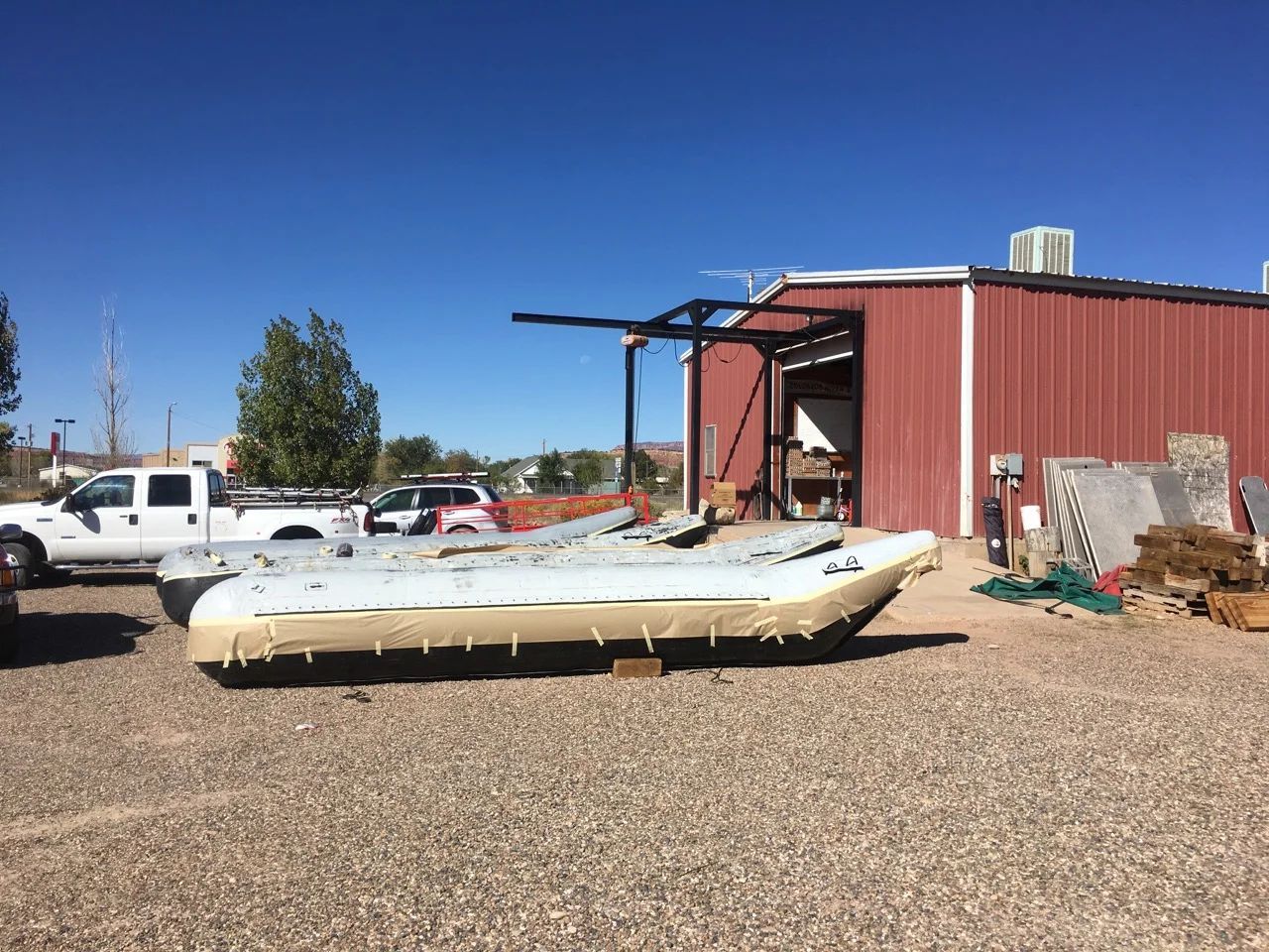 A rundown boat in a gravel lot with a red building and a white truck.