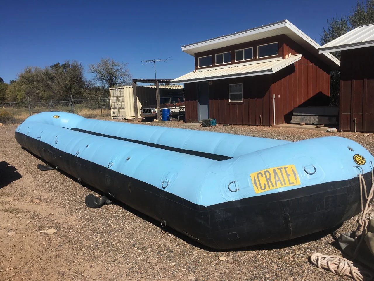 Blue and black inflatable raft on gravel, with a building in the background.