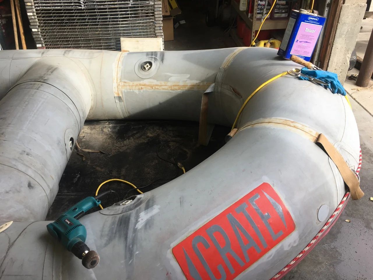 Gray inflatable raft being repaired; drill, glue and tools visible.