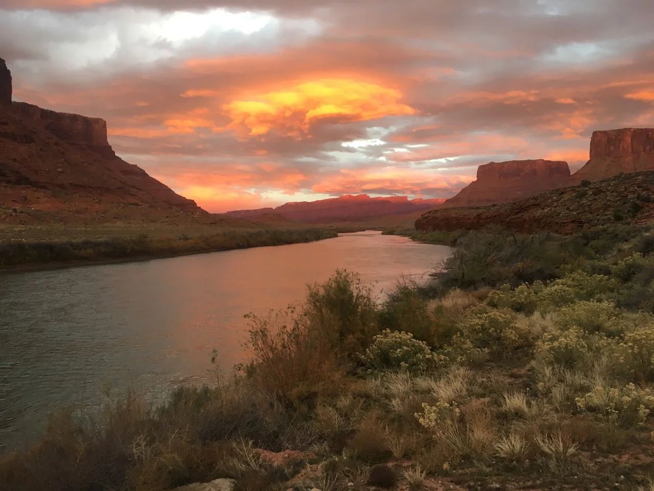 Sunset over river between sandstone cliffs, orange and red clouds reflected in water.