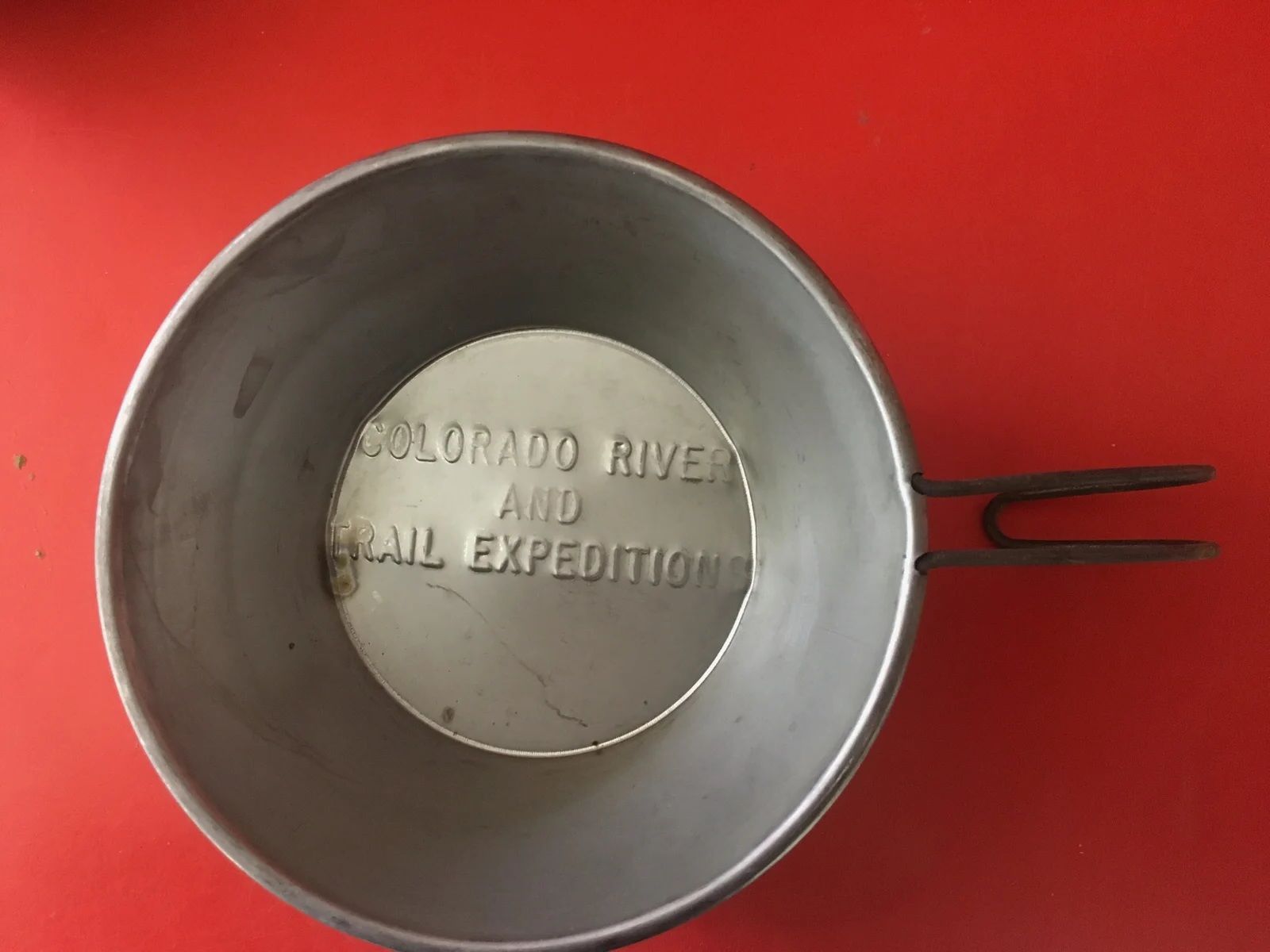 Silver metal camping cup with handle. Text inside reads
