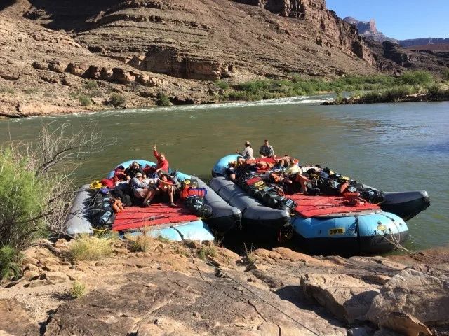 Two rafts with people on a riverbank, near a canyon.