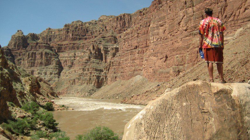 Person in red shirt looks out at a river in a canyon.