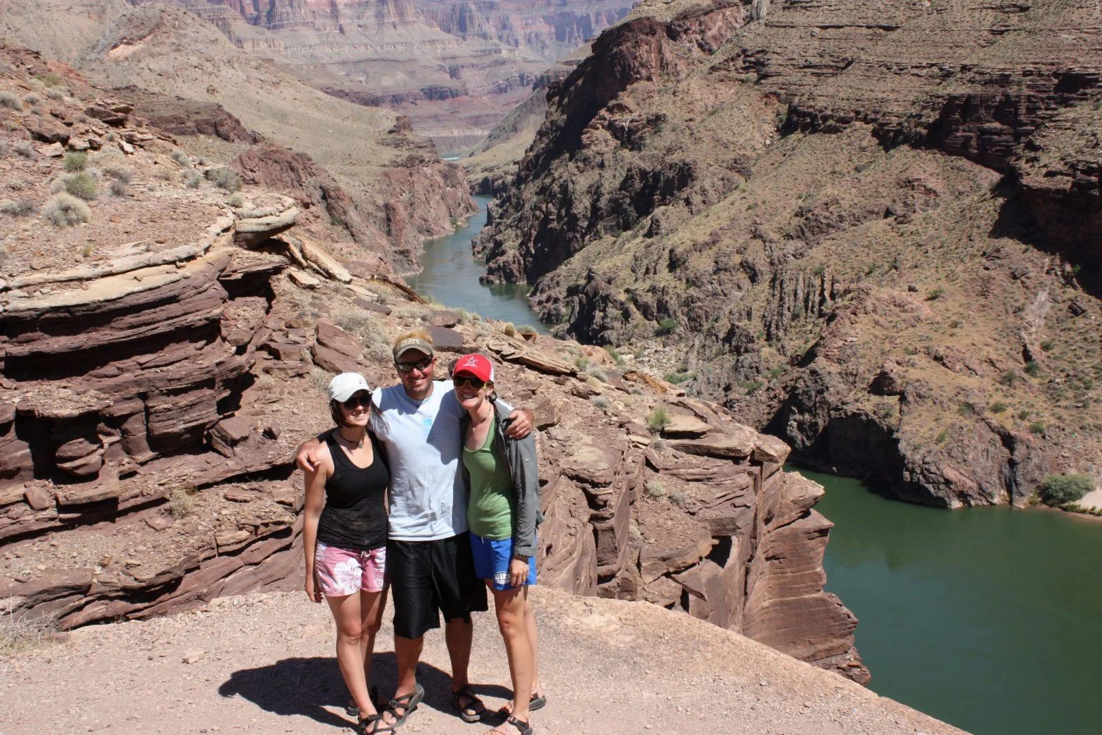 Three people pose on a cliff overlooking a canyon and river.