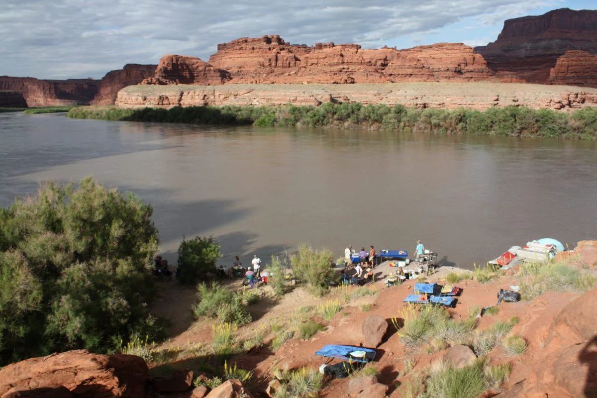 River with boats and people near red rock cliffs.