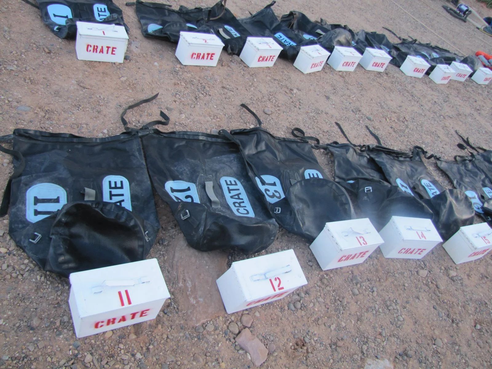 Black bags and numbered white crates arranged on dirt.