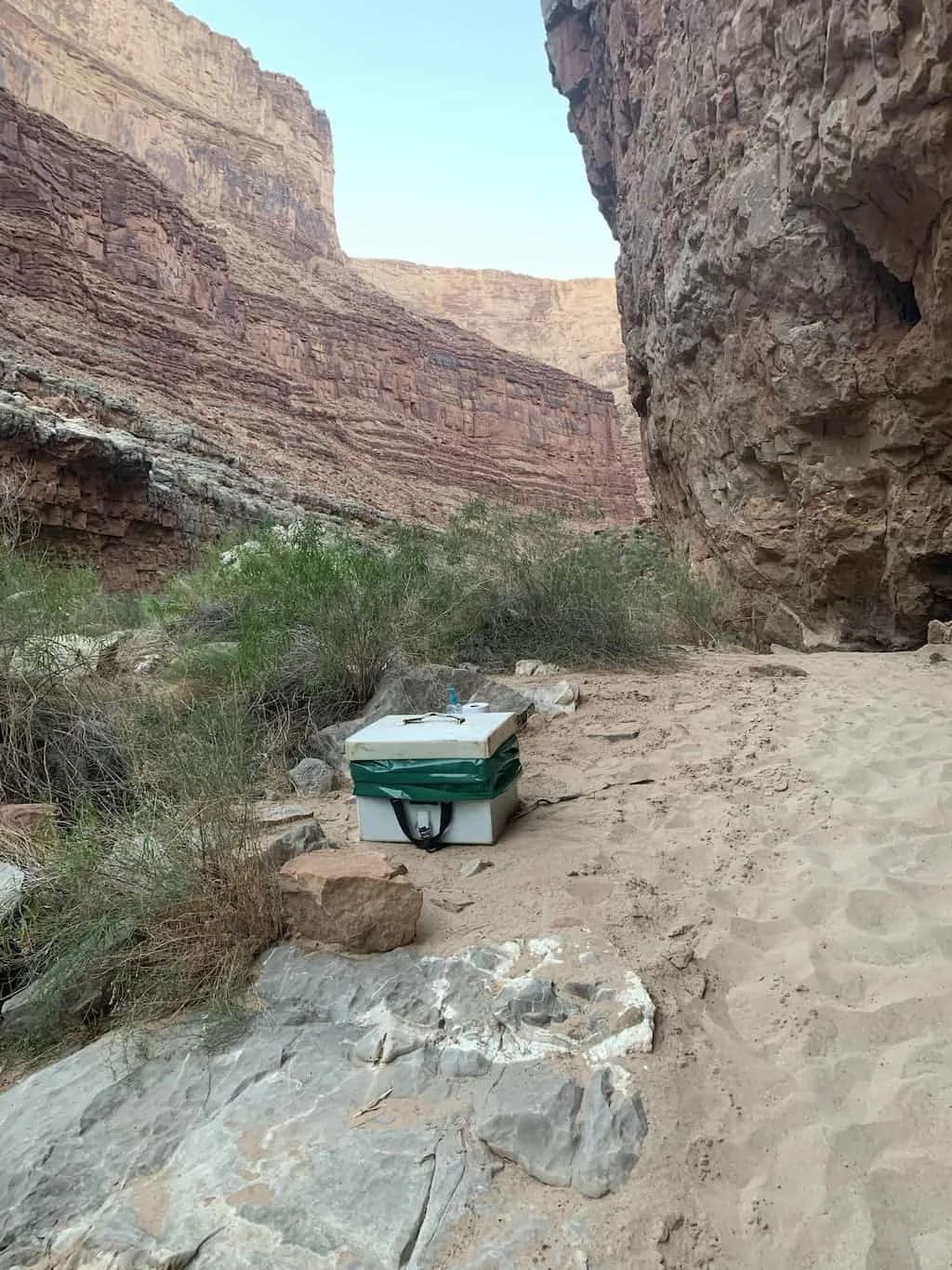 Beehive box on a sandy path in a canyon, near rocky walls and vegetation.
