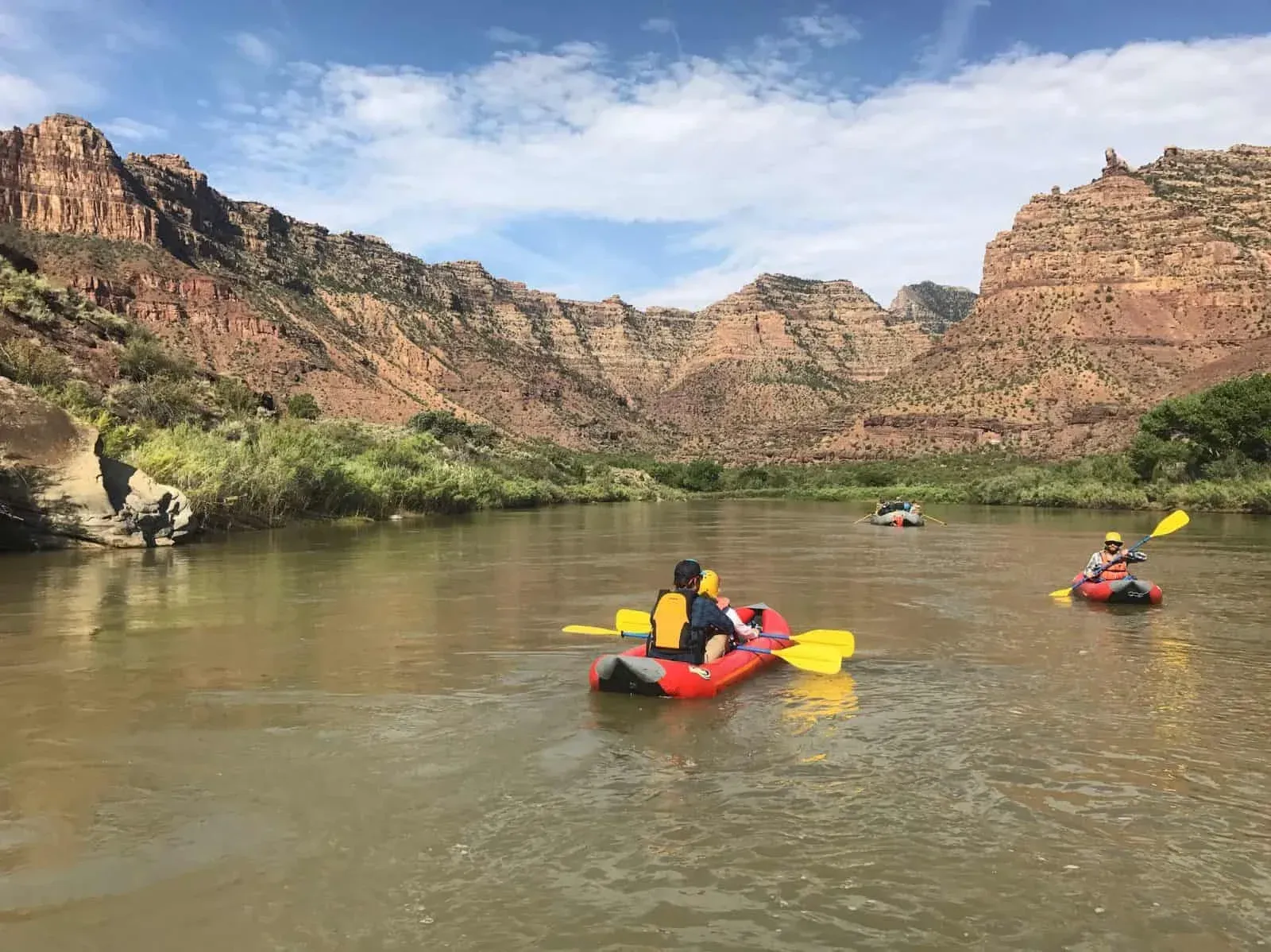 Kayakers paddling on a river between red rock canyon walls under a blue sky.