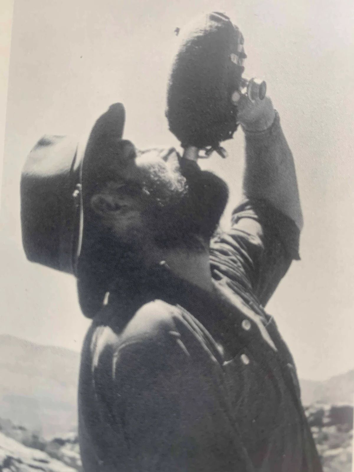 Man tilting his head back to drink from a gourd, wearing a hat, outdoors.