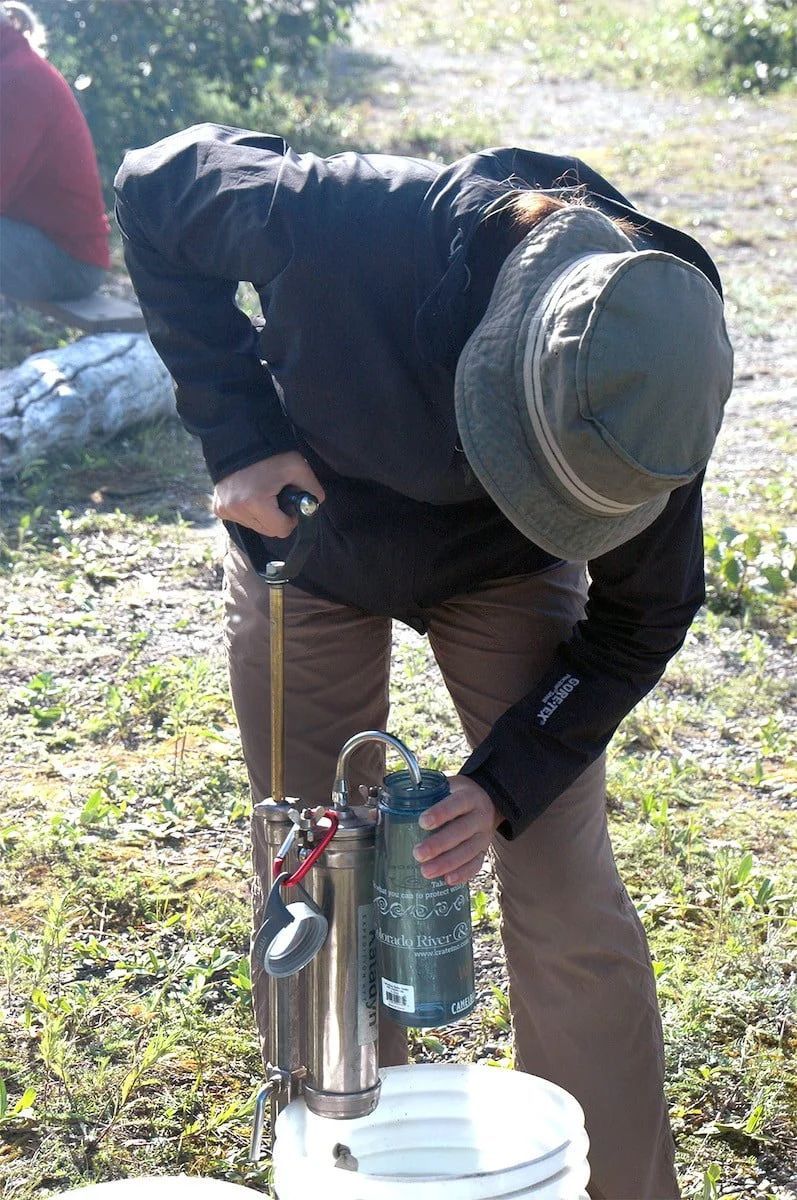 Person pumping water from a device into a bucket outdoors.