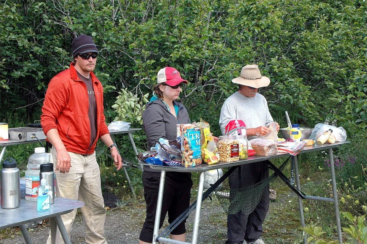 People at a food table outdoors; snacks and drinks on display. Trees in background.