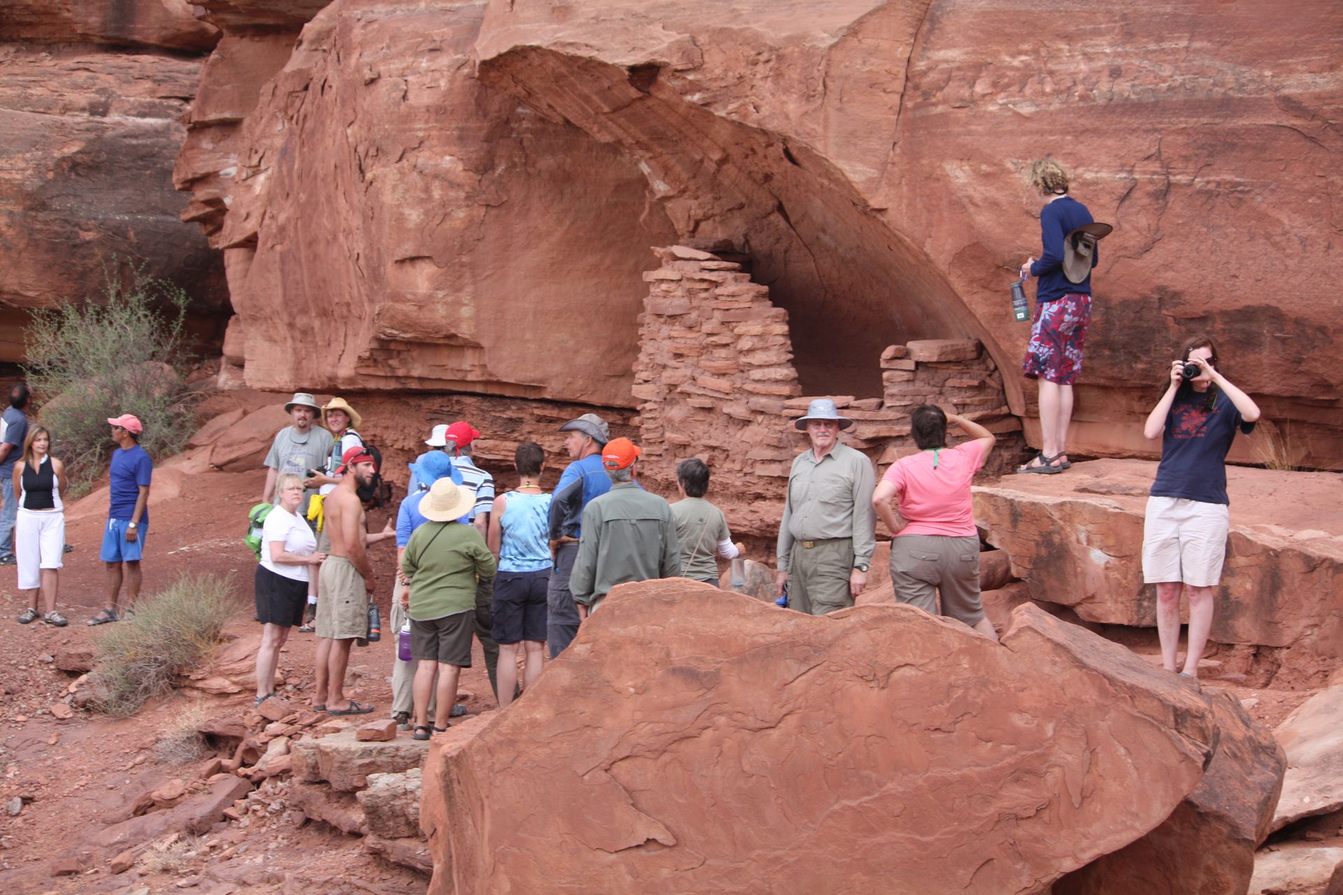 Group of people looking at a small stone structure in a red rock canyon.