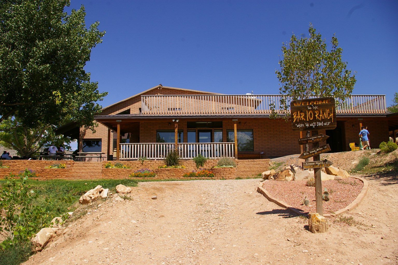Wooden lodge with porch, sign, gravel path, and blue sky.