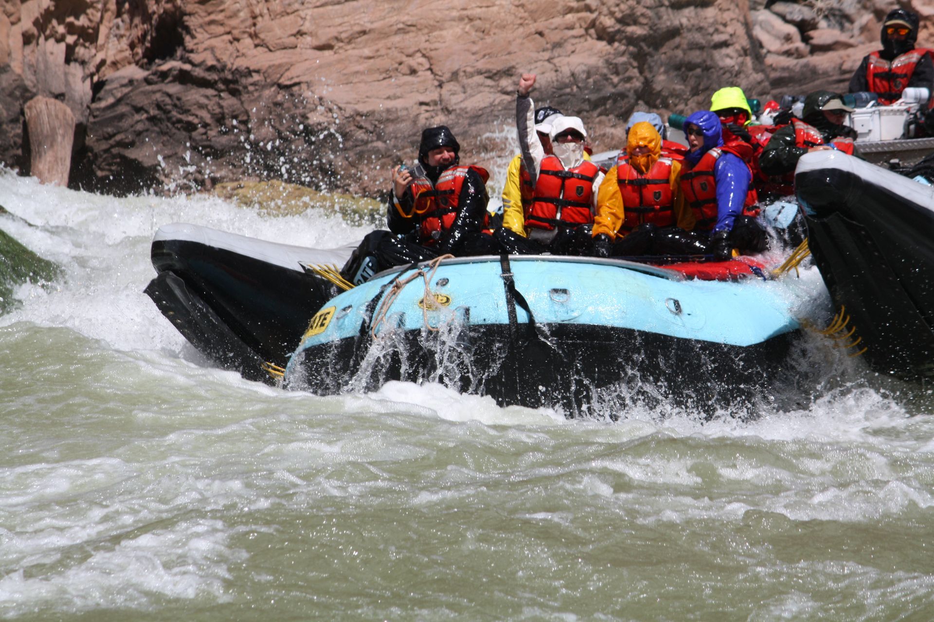 Rafting in a whitewater rapid; people in life vests navigate through splashing water.