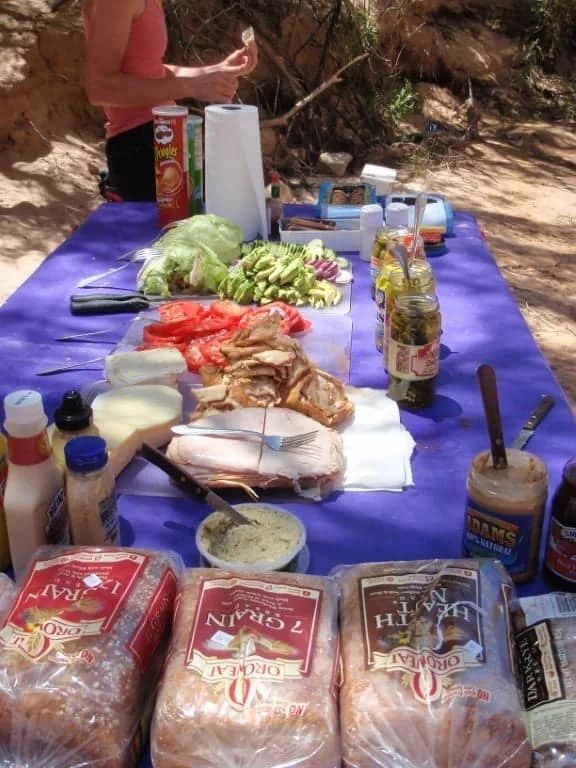 Picnic table with food and a person preparing sandwiches.