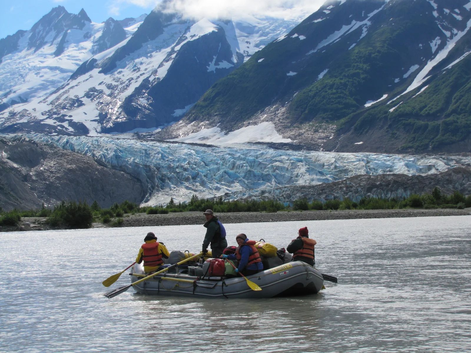 Rafting on a glacial river with snow-capped mountains and a glacier in the background.