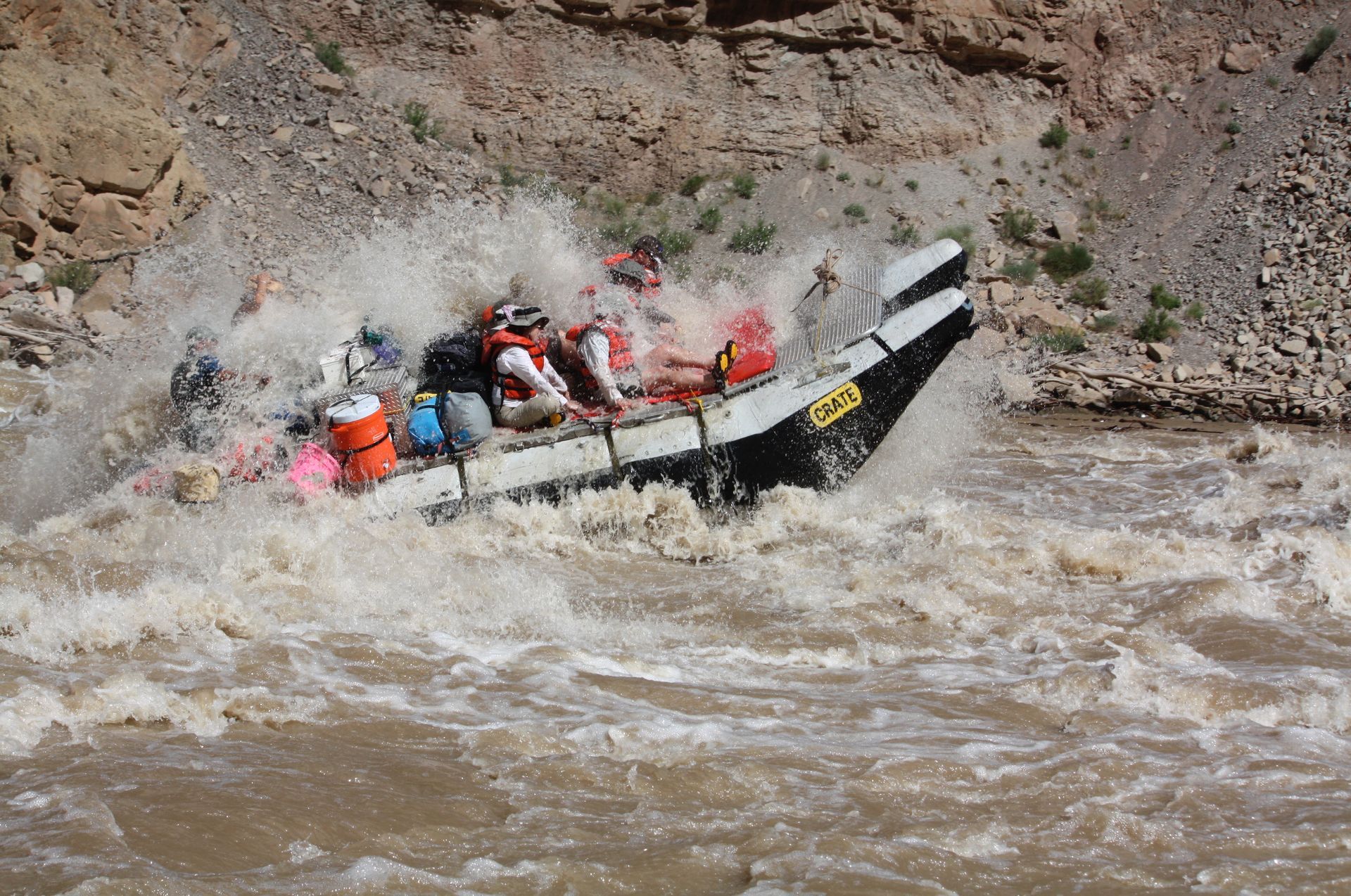 Rafting boat navigating rapids, white water splashing. People in life vests. Rocky canyon setting.