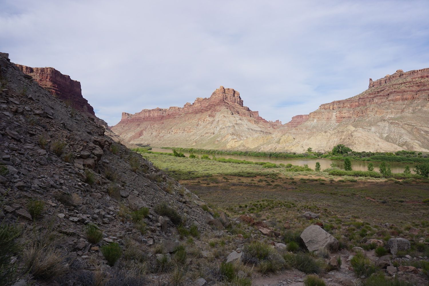 Canyon landscape with red rock formations and green vegetation under a cloudy sky.