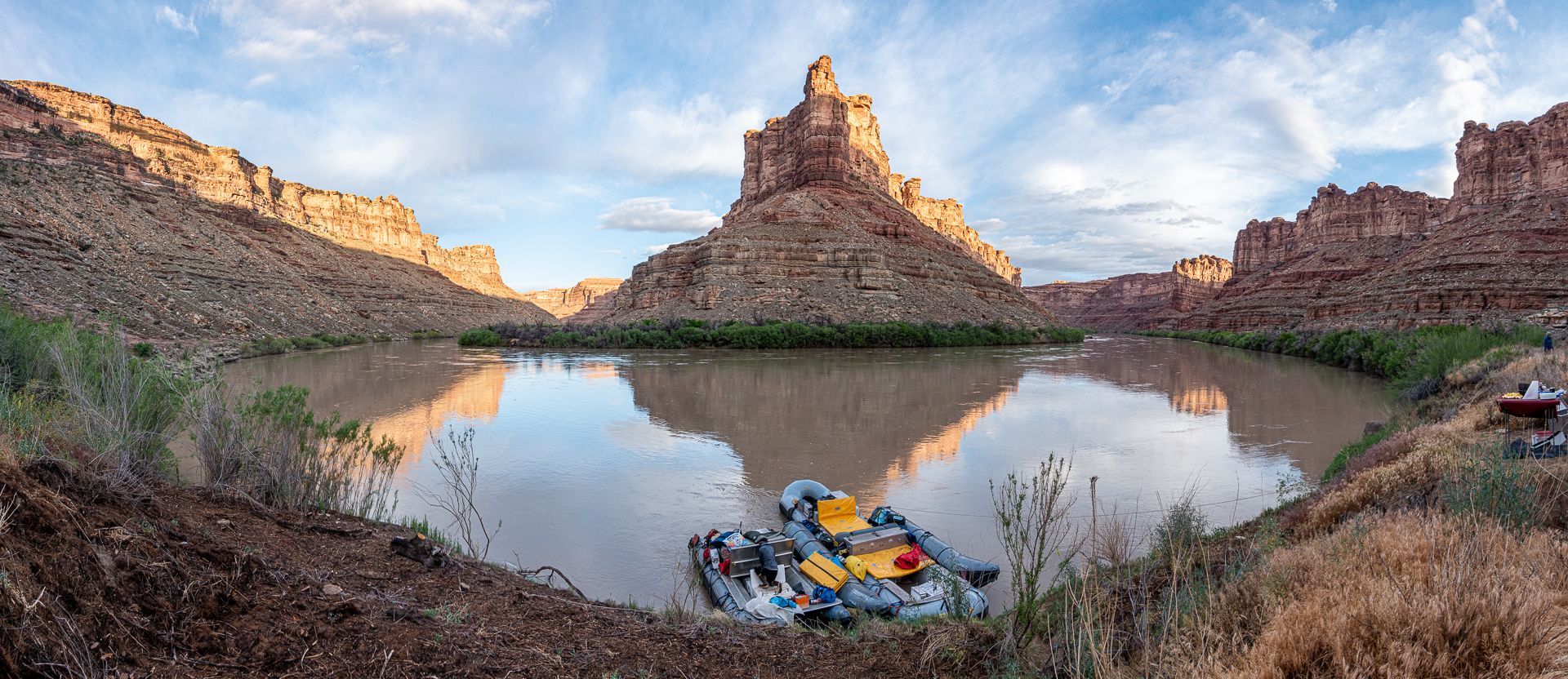 A serene river scene with a towering rock formation reflecting in the water, flanked by canyon walls.
