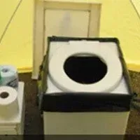 Portable toilet inside a tent. The toilet has a white seat and a black container. Rolls of toilet paper sit beside it.