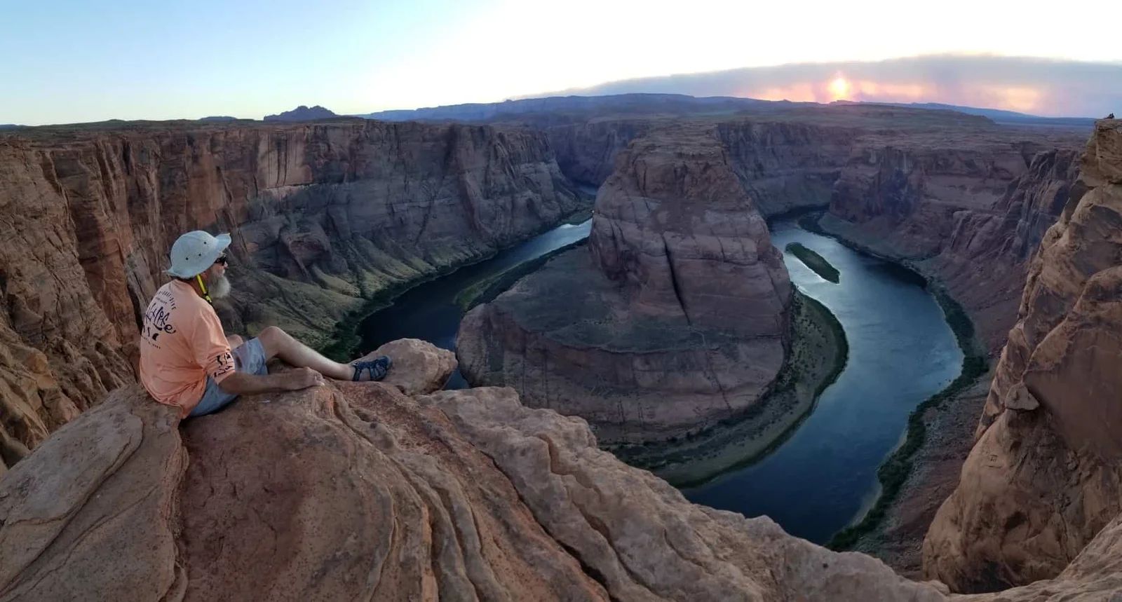 Person sitting on rock ledge overlooking Horseshoe Bend, Colorado River.