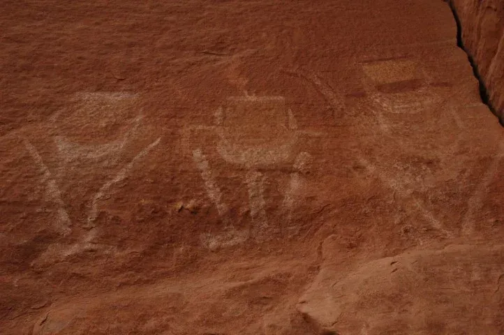 Petroglyphs carved into reddish sandstone. Three figures with geometric shapes and lines.
