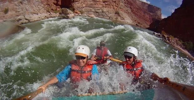 Whitewater rafters navigate a rapid, paddling amidst churning water, steep canyon walls in background.