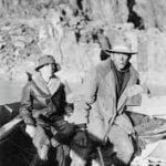 Two people in hats and coats, seated outdoors near rocky terrain.