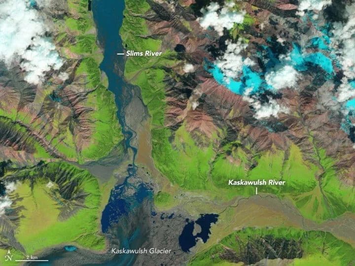 Satellite view of a river, glacier, and mountains. Green, brown, and blue colors dominate the landscape.