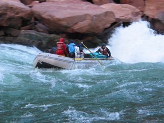 Whitewater raft navigating rapids in a rocky river; splashing water, red and blue jackets visible.