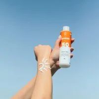 A person's arm applying sunscreen in the shape of a sun against a blue sky.