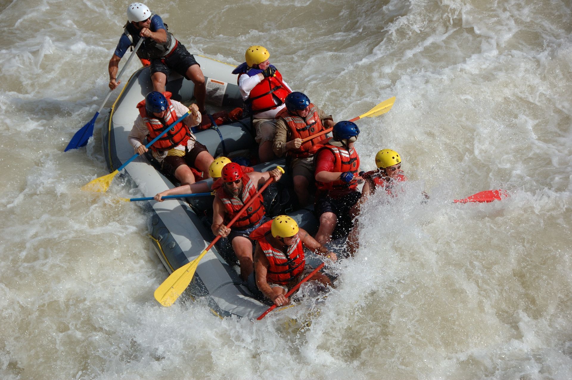 Rafting on a whitewater river; people in helmets and life vests paddle through turbulent, foamy water.