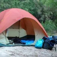 Orange and tan camping tent set up outdoors, with sleeping bag, blue bag and boots.