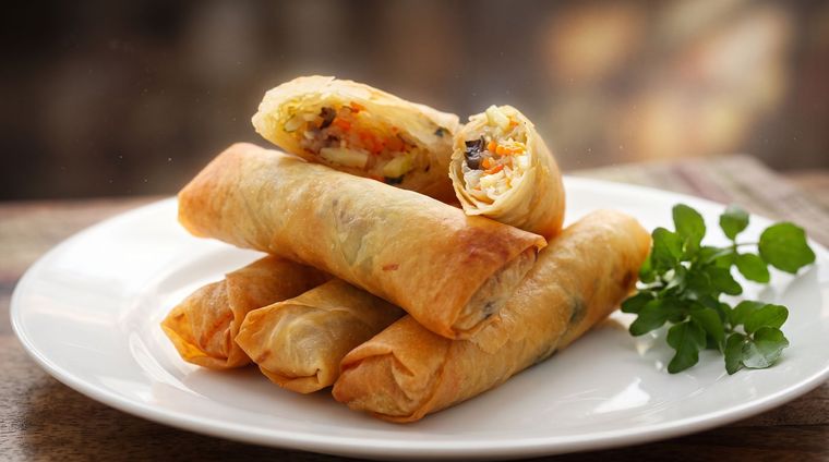Plate of crispy spring rolls with dipping sauce and parsley garnish on a table