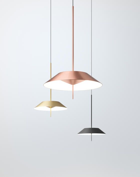 Tres modernas lámparas colgantes en cobre, oro y gris oscuro cuelgan sobre un fondo gris claro.