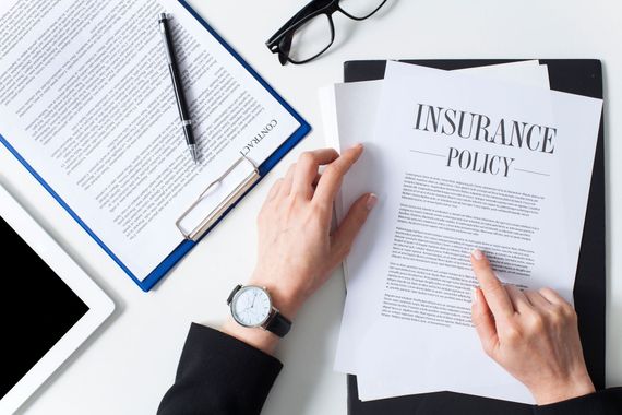 Person reviewing an insurance policy document on a desk with a clipboard, pen, tablet, and glasses nearby.