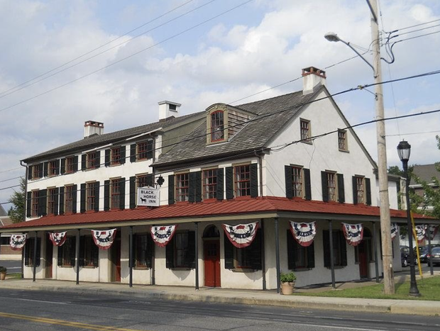 A black car is driving down the street in front of a large building.