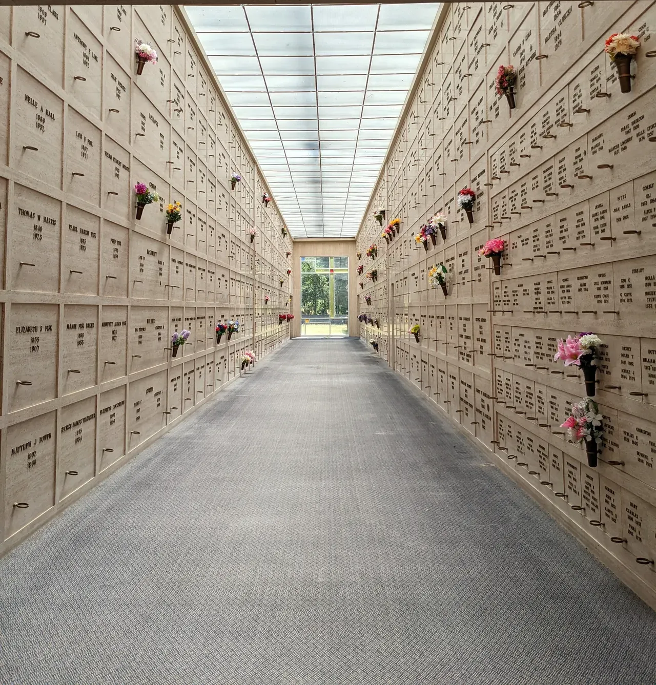 Indoor columbarium with rows of niches, some holding flowers.