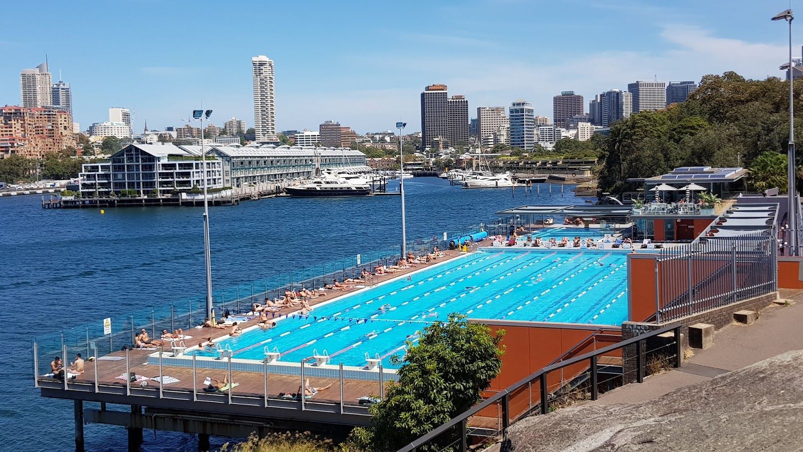 A large swimming pool is surrounded by water and a city in the background.